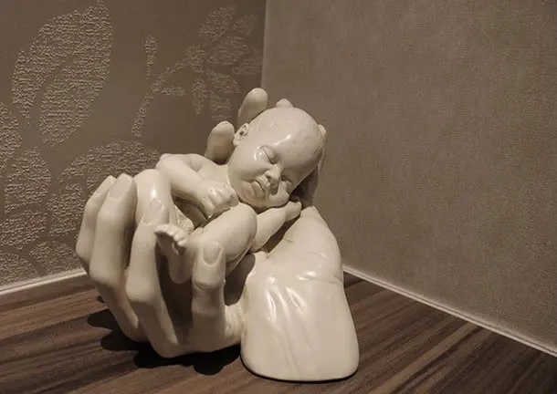A porcelain sculpture of hands cradling a sleeping baby